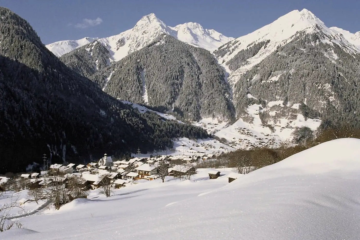Verschneites Dorf im Hochmontafon, darüber die Gipfel im Winterlicht